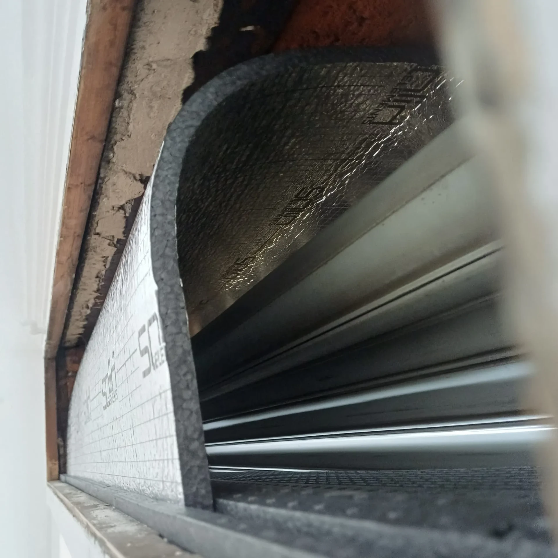 Photo d'intervention Reparrenov : pose d'un panneau isolant dans le caisson d'un volet roulant, vue depuis l'intérieur du coffre